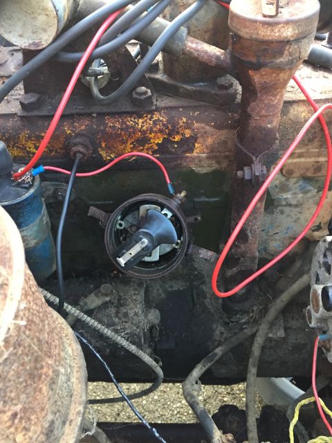 1946 Jeep Willys - A close-up view of the distributor cap and rotor assembly on a rusty engine. Red spark plug wires are visible, connected to the distributor…