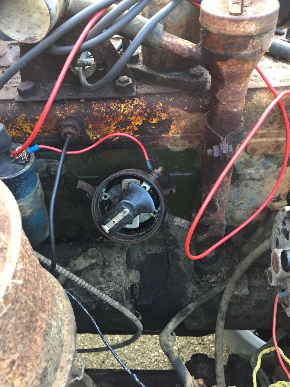Close-up of a rusty engine distributor cap and rotor with red spark plug wires.