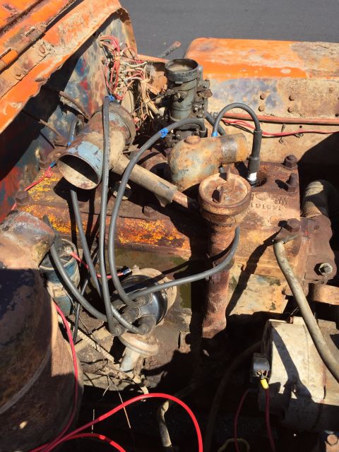 1946 Jeep Willys - A close-up view of a rusty, orange engine bay with various components visible, including a carburetor, spark plug wires, and a distributor.…