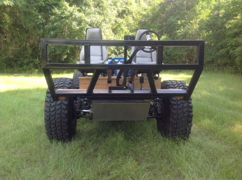 1992 Ford Bronco - The rear view of a custom-built, two-seater off-road vehicle with large tires and a metal roll cage. The vehicle is parked on a grassy fiel…