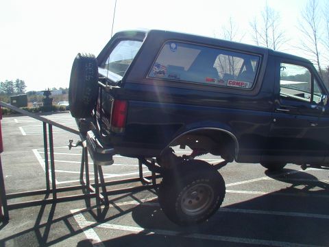 1988 Ford Bronco - A dark blue Ford Bronco is elevated on a lift, showing its undercarriage and suspension components.