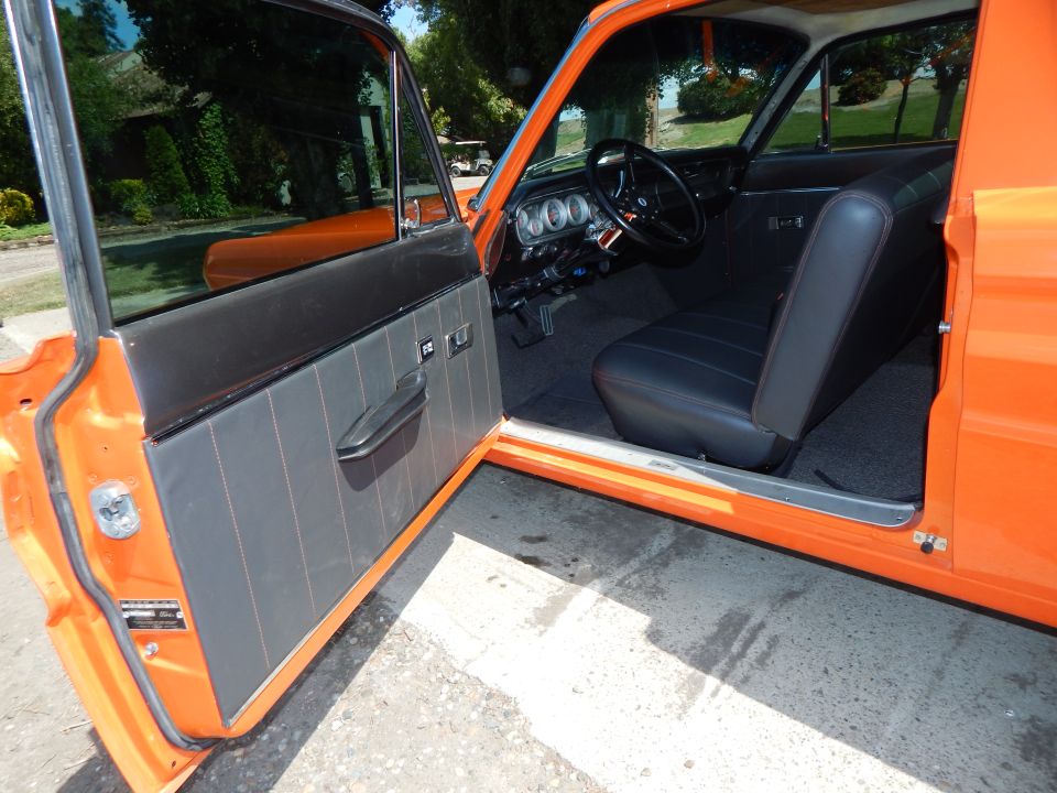 Interior of an orange 1964 Ford Ranchero with driver's door open, showing gray door panel and black seat with orange stitching.
