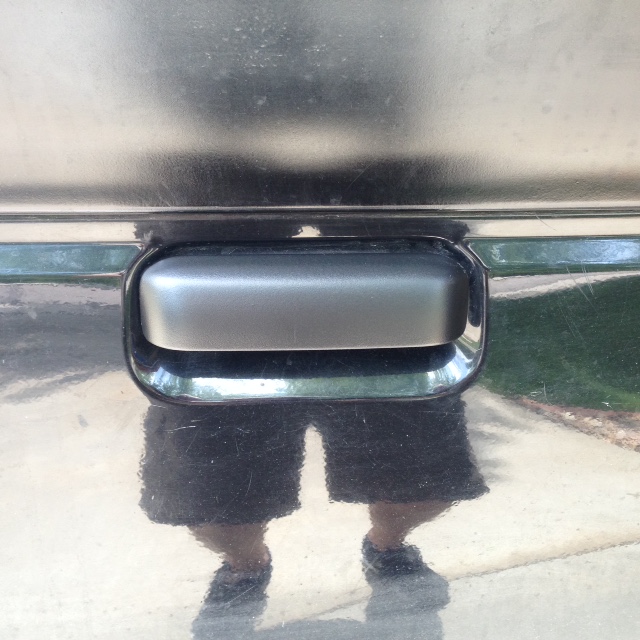 Black tailgate handle on a vehicle with reflection of legs and shorts.