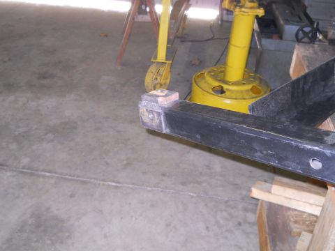 1992 Ford Bronco - A close-up view shows the welded end of a black metal frame, likely a vehicle part, resting on wooden supports. A yellow industrial machine…