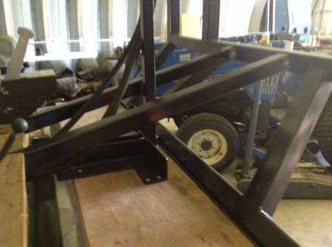 1992 Ford Bronco - A close-up view of a black metal fabrication attached to a wooden surface, with a blue tractor visible in the background. The fabrication i…