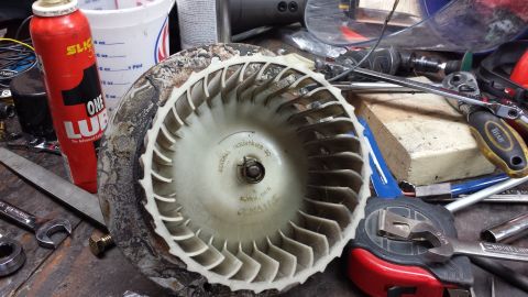 1978 Ford Bronco - A dirty blower wheel assembly sits on a workbench surrounded by tools, including a can of lubricant, wrenches, and a tape measure.
