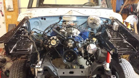 1978 Ford Bronco - The engine bay of a classic Ford Bronco is shown, with the engine partially assembled and painted blue. The vehicle is in a garage setting…