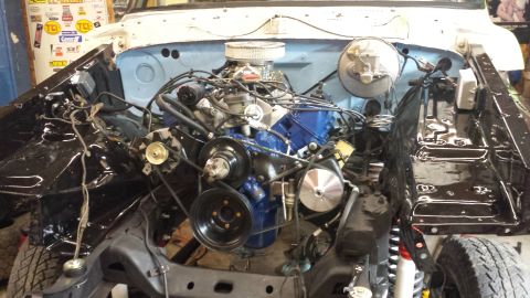 1978 Ford Bronco - The engine bay of a vehicle undergoing restoration or modification, featuring a blue engine block, carburetor, and various hoses and belts.