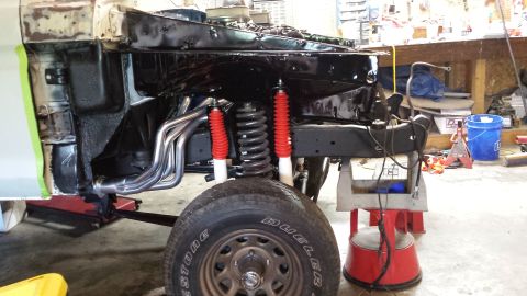 1978 Ford Bronco - The front suspension and engine bay of a classic Ford Bronco are visible, featuring new red-booted shock absorbers, chrome exhaust headers,…