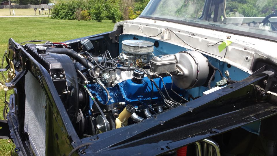 Classic Ford truck engine bay with blue engine, chrome air cleaner, and radiator.