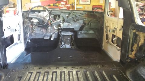 Interior of a classic Ford Bronco during restoration, showing dashboard, steering wheel, pedals, and black coa
