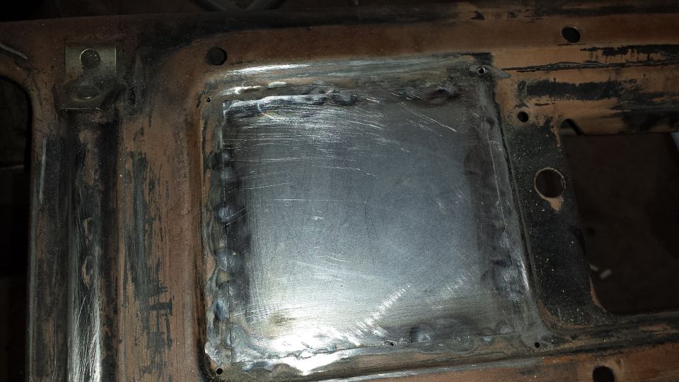 Welded metal patch panel on a rusted vehicle frame.