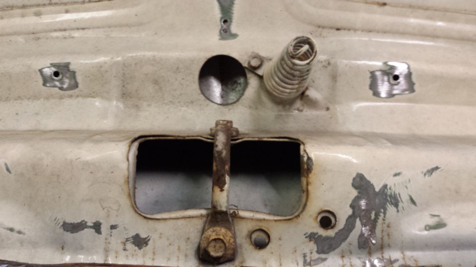 Underside of vehicle hood/trunk with latch, spring, and rust.