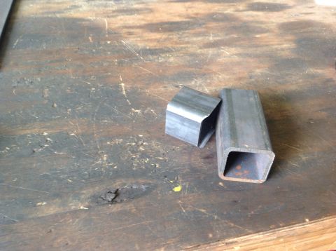 1992 Ford Bronco - Two cut pieces of square metal tubing are shown on a worn wooden surface. One piece is shorter and angled, while the other is longer and op…
