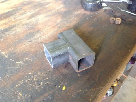 1992 Ford Bronco - Two pieces of square metal tubing are joined at a right angle on a wooden workbench. Tools and other hardware are visible in the background.