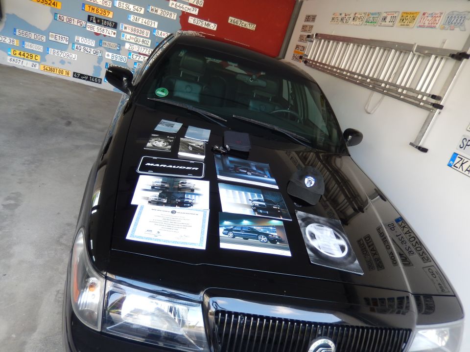 Black Mercury Marauder with documents on hood, license plates on wall.