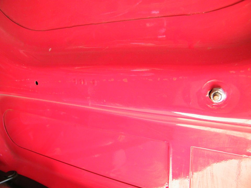 Close-up of a red vehicle interior with a bolt and a small hole.