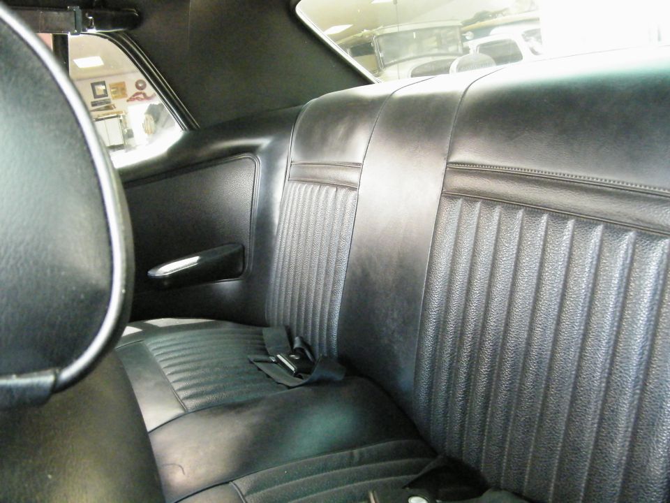 Interior of a classic car showing black vinyl bucket seats and rear seat.