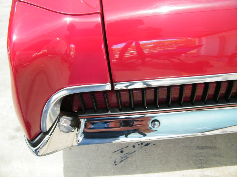 Close-up of the rear of a red classic car, showing chrome bumper and taillight detail.