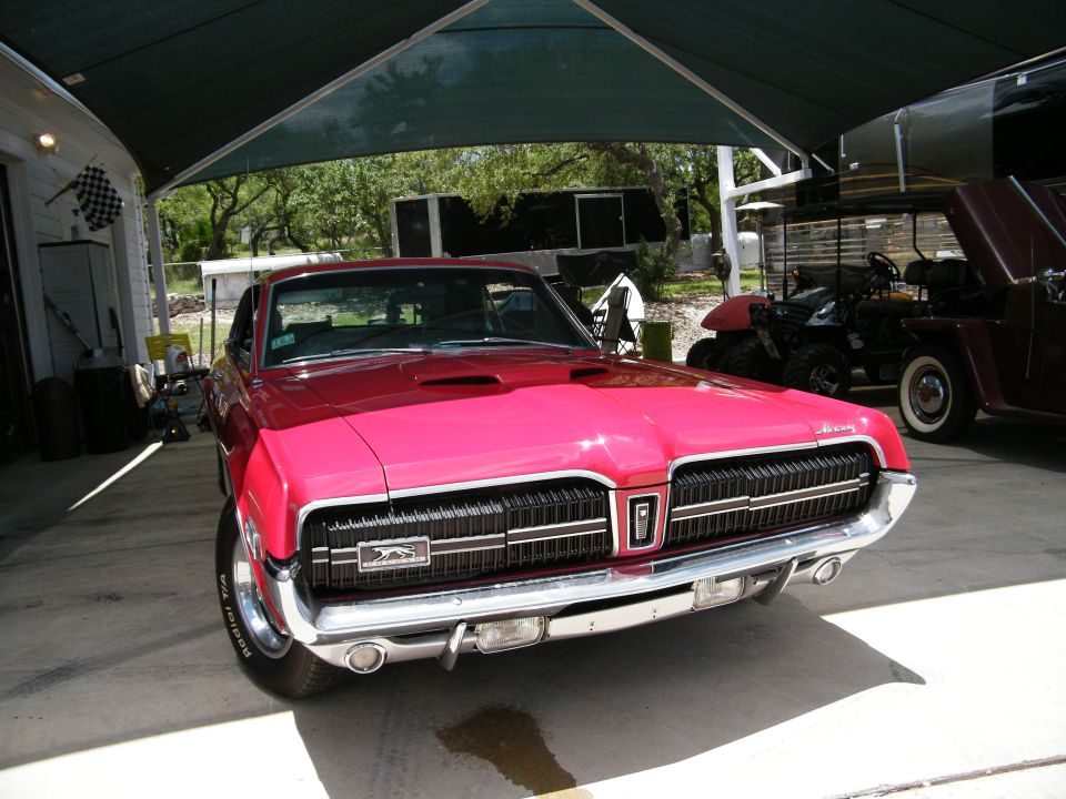 1968 Mercury Cougar in bright pink, front view under a green awning.