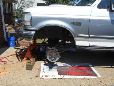 1994 Ford Bronco - A white and silver Ford Bronco is parked outdoors with its front end raised on jack stands, revealing the suspension and brake components.…