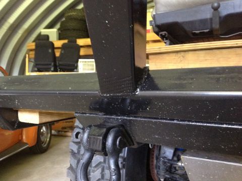 1992 Ford Bronco - A close-up view of a black metal frame with welded joints, featuring two black tow shackle mounts attached to the underside. The frame appe…