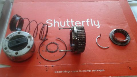 1996 Ford Bronco - Disassembled parts of a manual locking hub are laid out on a red cardboard surface. Visible parts include the main hub body with "LOCK" and…
