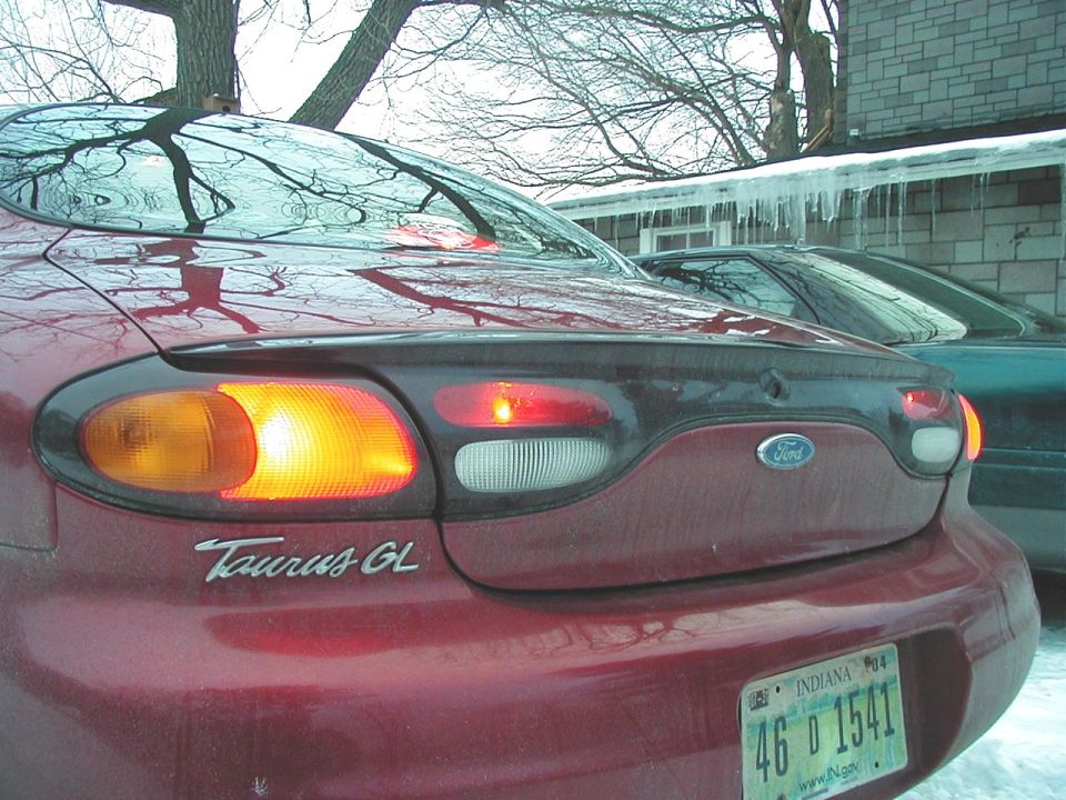 Red 1997 Ford Taurus GL with illuminated taillights, another car behind it
