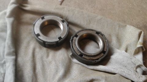 1996 Ford Bronco - Two metal lock nuts with internal threading are shown resting on a beige cloth. The nuts have a segmented outer edge with notches for tool…