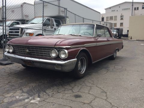 1968 Ford Mustang - A classic maroon 1961 Ford Galaxie coupe is parked in an outdoor lot, with commercial trucks visible in the background.