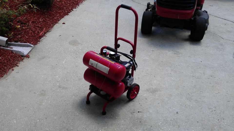 Red portable air compressor with two stacked tanks and wheels on concrete