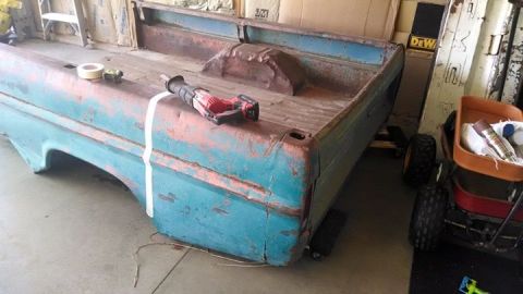 1994 Ford Bronco - A weathered blue truck bed sits in a workshop, prepped for work with tape and a saw.