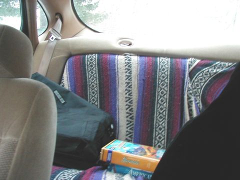 1997 Ford Taurus - The interior of a vehicle shows a blanket draped over the back seat, a black bag, and a VHS tape on the floor.