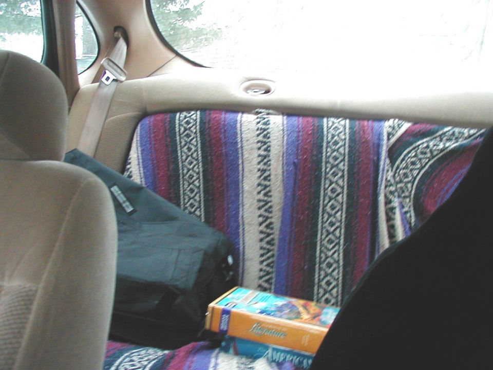 Interior of a car with a patterned blanket on the back seat, a black bag, and a VHS tape
