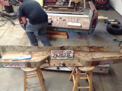 1994 Ford Bronco - A rusty bumper with a Wisconsin license plate and two stickers is displayed on stools in a workshop.
