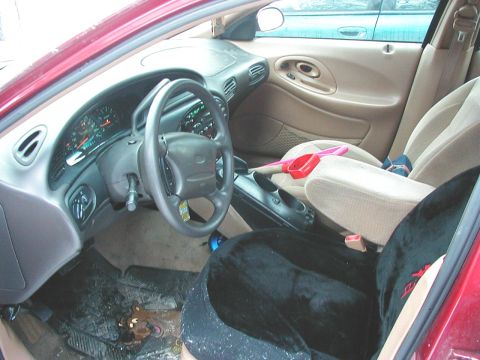 1997 Ford Taurus - The interior of a 1997 Ford Taurus shows tan seats, a black seat cover, and the dashboard with gauges.