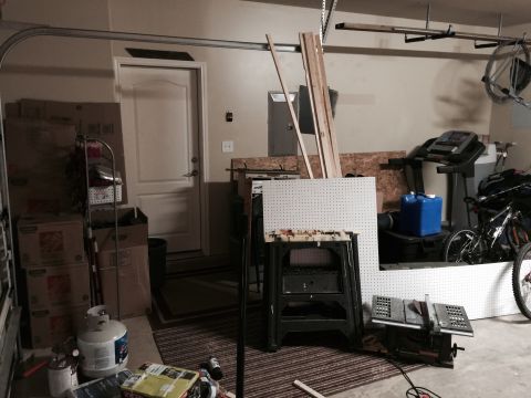 2015 Ford Deluxe - A cluttered garage scene includes a workbench, table saw, treadmill, and a bicycle, with various storage boxes and lumber.