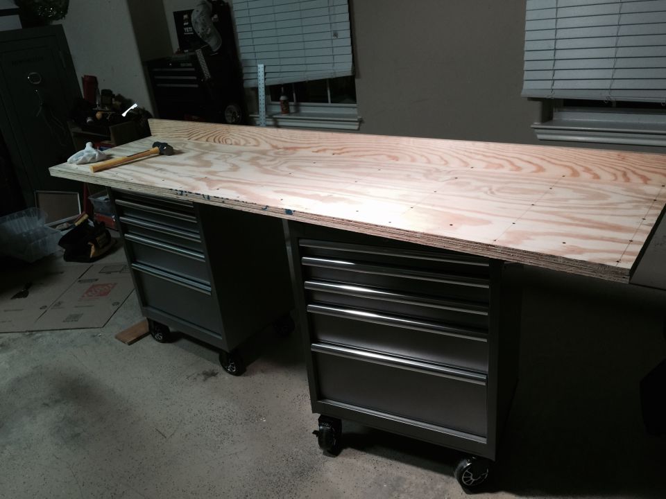 Workbench with plywood top over two rolling tool chests. Hammer and cloth on top