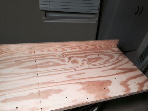 2015 Ford Deluxe - A sheet of plywood with markings and holes is shown in a room with blinds and cabinets.