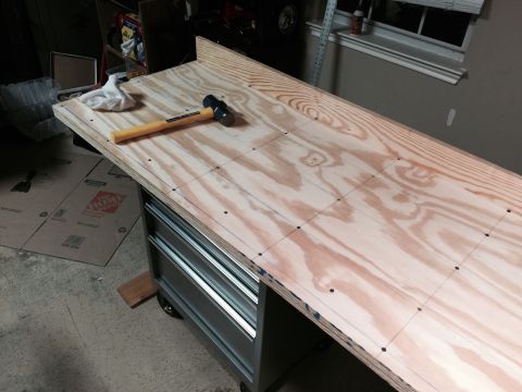 2015 Ford Deluxe - A workbench surface is marked with a grid of lines and dots, with a hammer and cloth resting on it.
