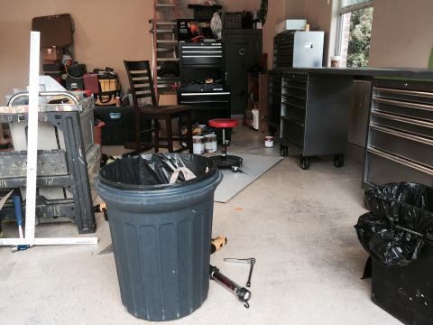 2015 Ford Deluxe - A cluttered garage scene with various tools, storage units, and a trash can in the foreground.