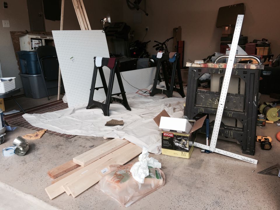Garage scene with lumber, pegboard, sawhorses, and tools on a concrete floor