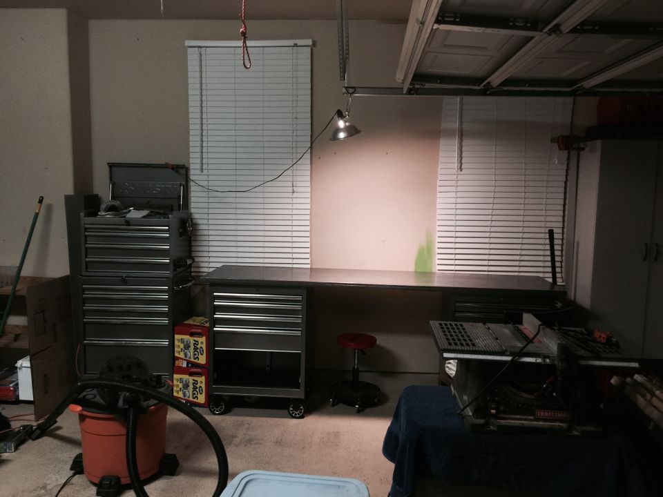 Garage interior with a long workbench, tool chests, a red stool, a table saw, and a shop vac