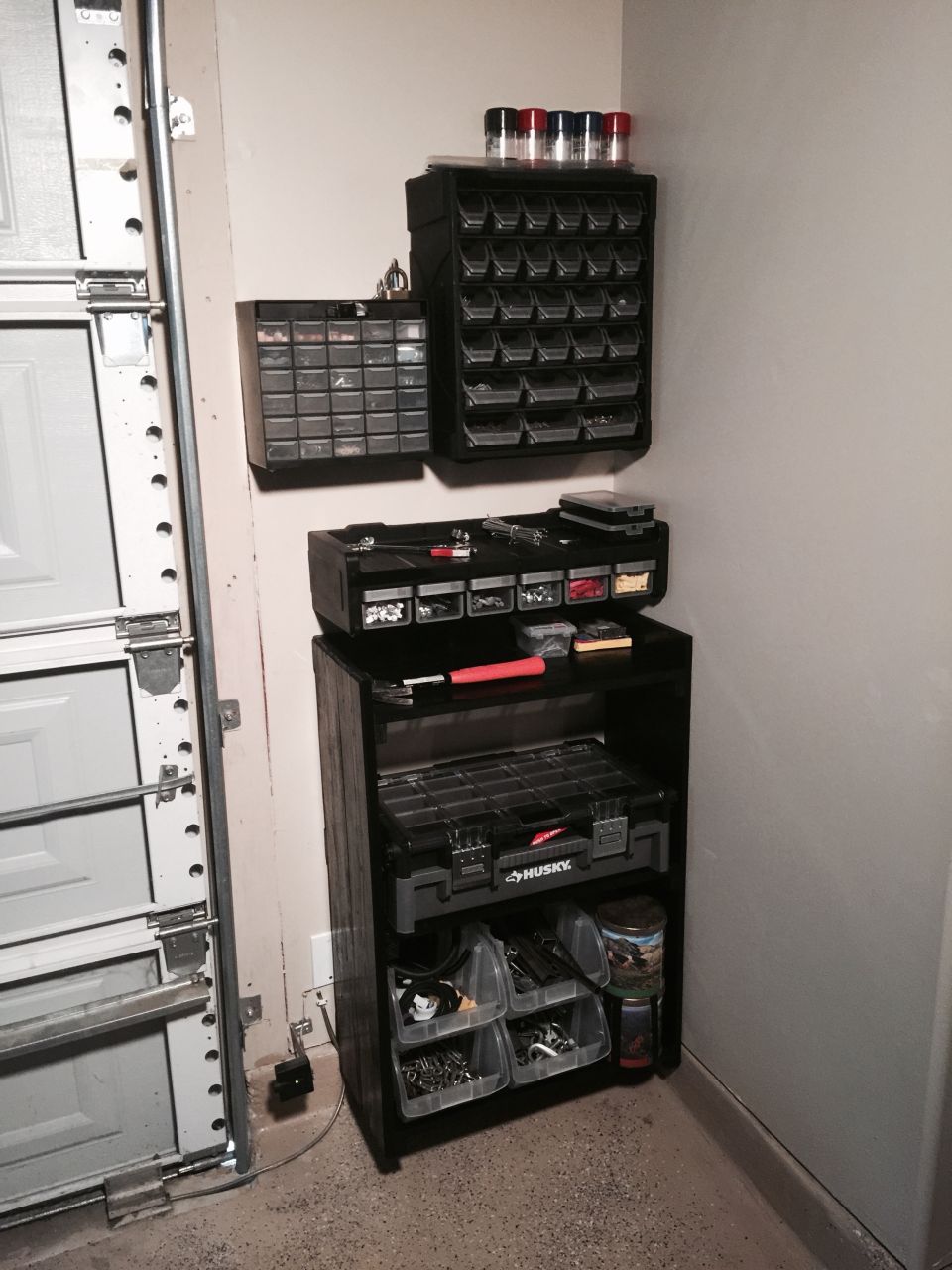 Shelving unit with many small parts bins, a Husky toolbox, and containers of hardware next to a garage door