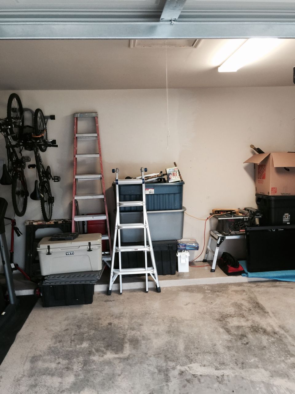 Garage interior with bicycles on wall mount, ladders, storage bins, and a cooler