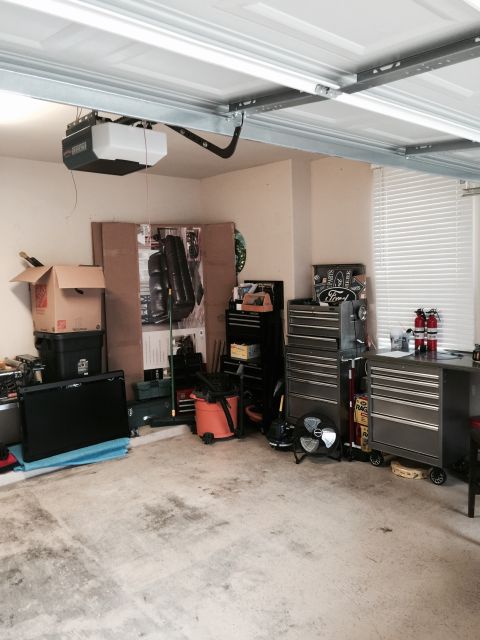 2015 Ford Deluxe - A cluttered garage scene with various tools, storage containers, and a prominent garage door opener.