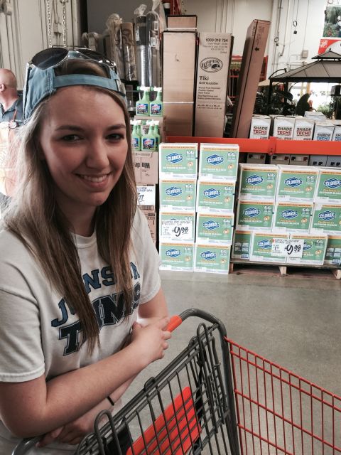 2015 Ford Deluxe - A woman smiles while pushing a shopping cart down an aisle stocked with household cleaning supplies.
