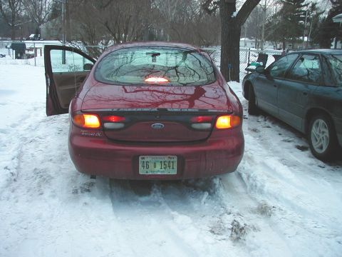 1997 Ford Taurus - Rear view of a red 1997 Ford Taurus parked in the snow with its driver's door open.