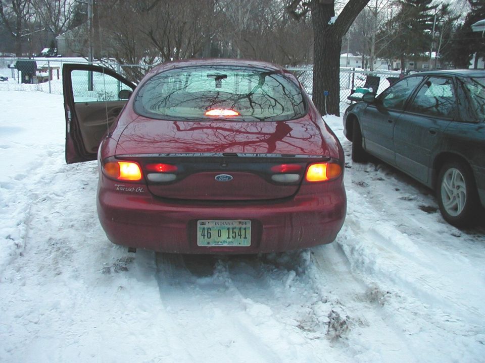 1997 Ford Taurus rear view in snowy driveway, driver door open. Another car is parked to the right