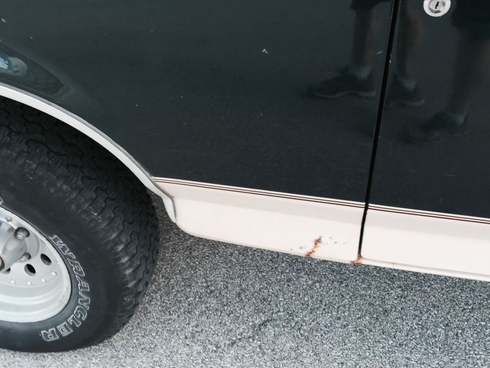 Side detail of black vehicle with tan lower panel, rust spots, and Goodyear Wrangler tire on alloy wheel